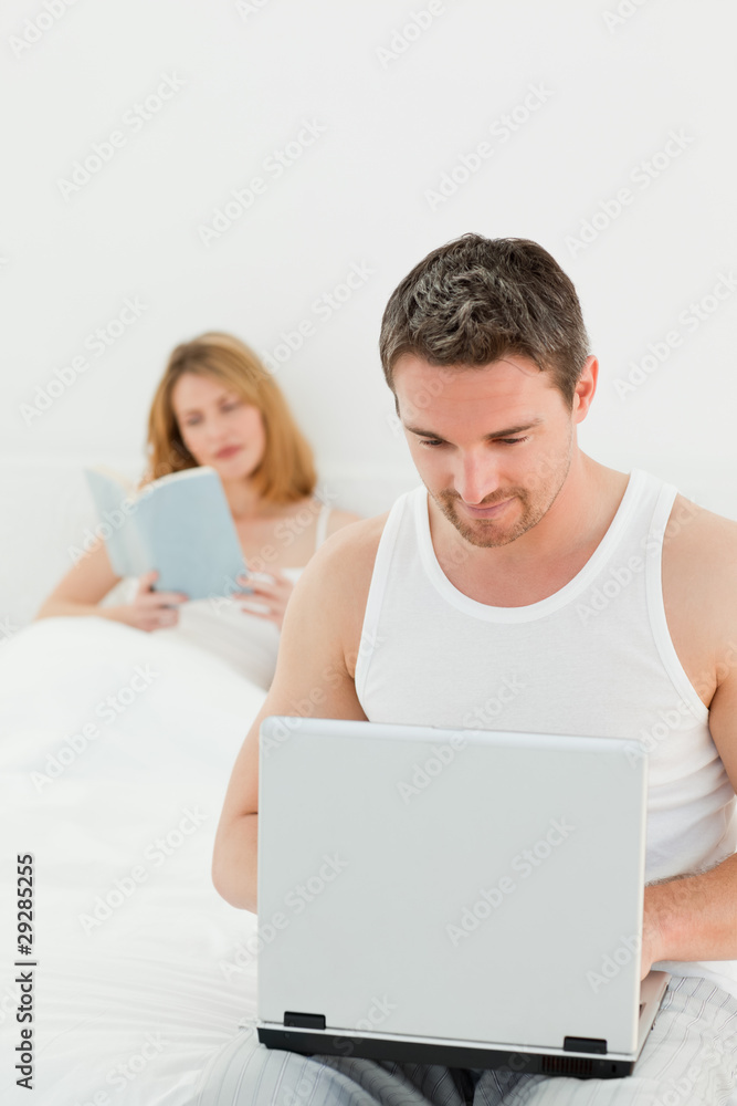 Man is on his laptop while his wife is reading a book Man is on his laptop while his wife is reading a book