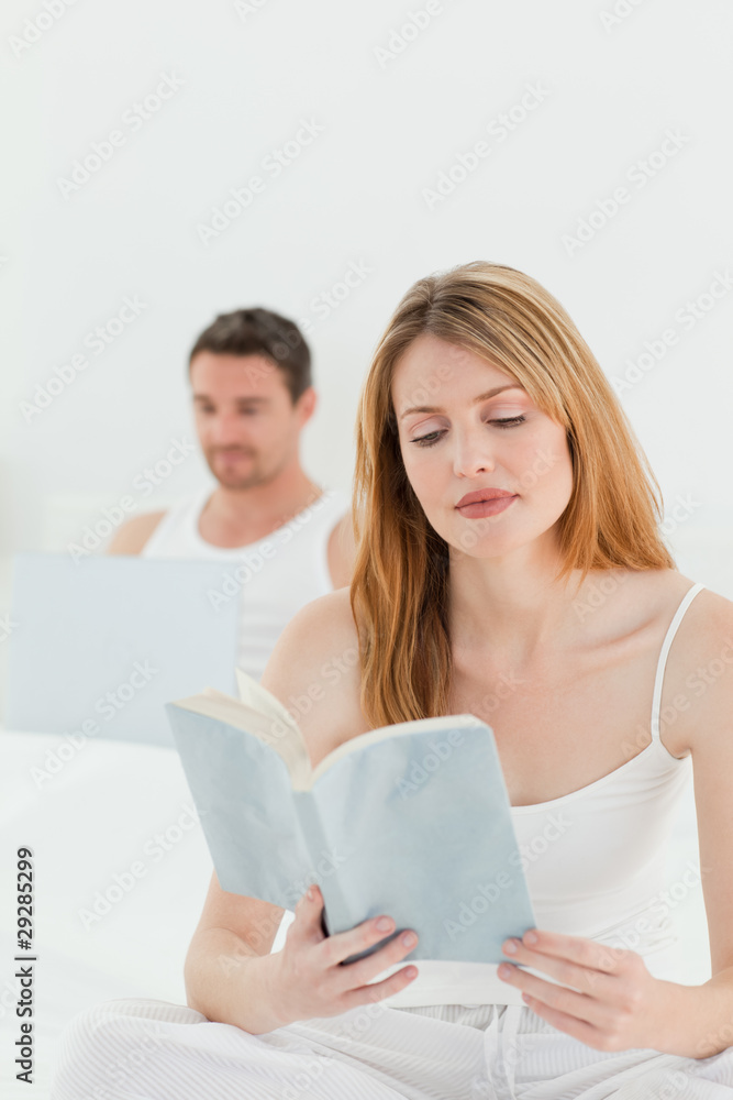 Man is on his laptop while his wife is reading a book Man is on his laptop while his wife is reading a book