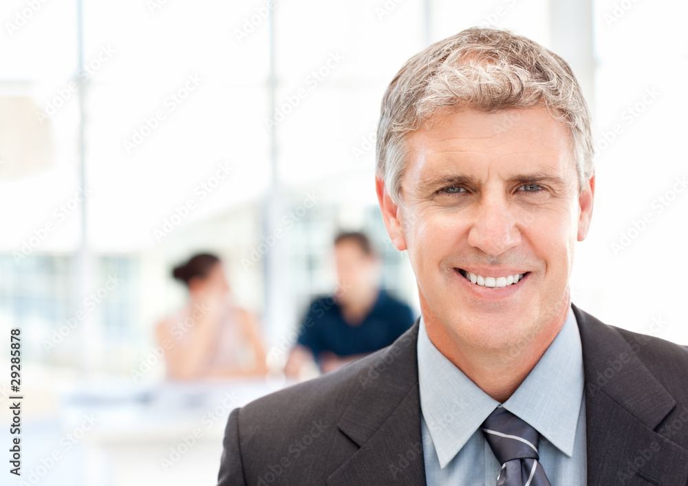 Businessman looking at the camera while their team is working Businessman looking at the camera while their team is working