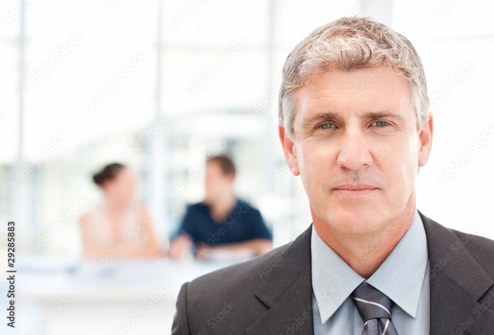 Businessman looking at the camera while his team is working Businessman looking at the camera while his team is working