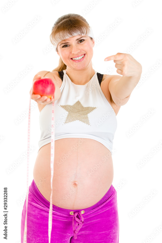 Smiling pregnant woman pointing finger at measure tape and apple Smiling pregnant woman pointing finger at measure tape and apple