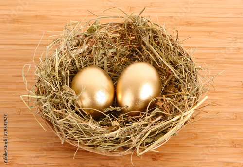 Three golden hen's eggs in the grassy nest on the wooden table