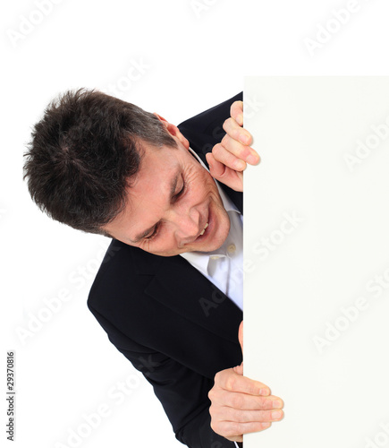 Bild auf Leinwand Attraktiver Mann schaut hinter weißen Wand hervor.