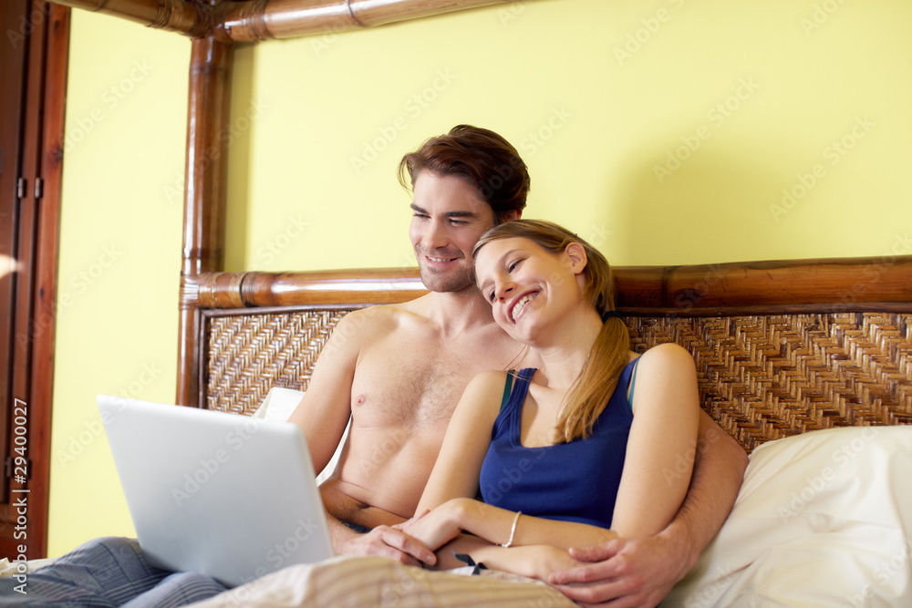 young couple lying on bed with pc young couple lying on bed with pc