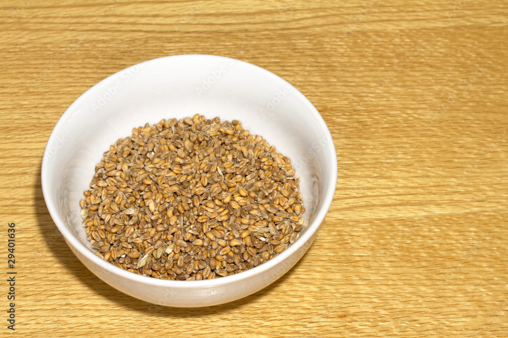 Bowl of wheat grain in white bowl on wooden table Bowl of wheat grain in white bowl on wooden table