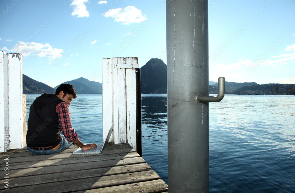 giovan ragazzo seduto su un pontile lavora al computer giovan ragazzo seduto su un pontile lavora al computer
