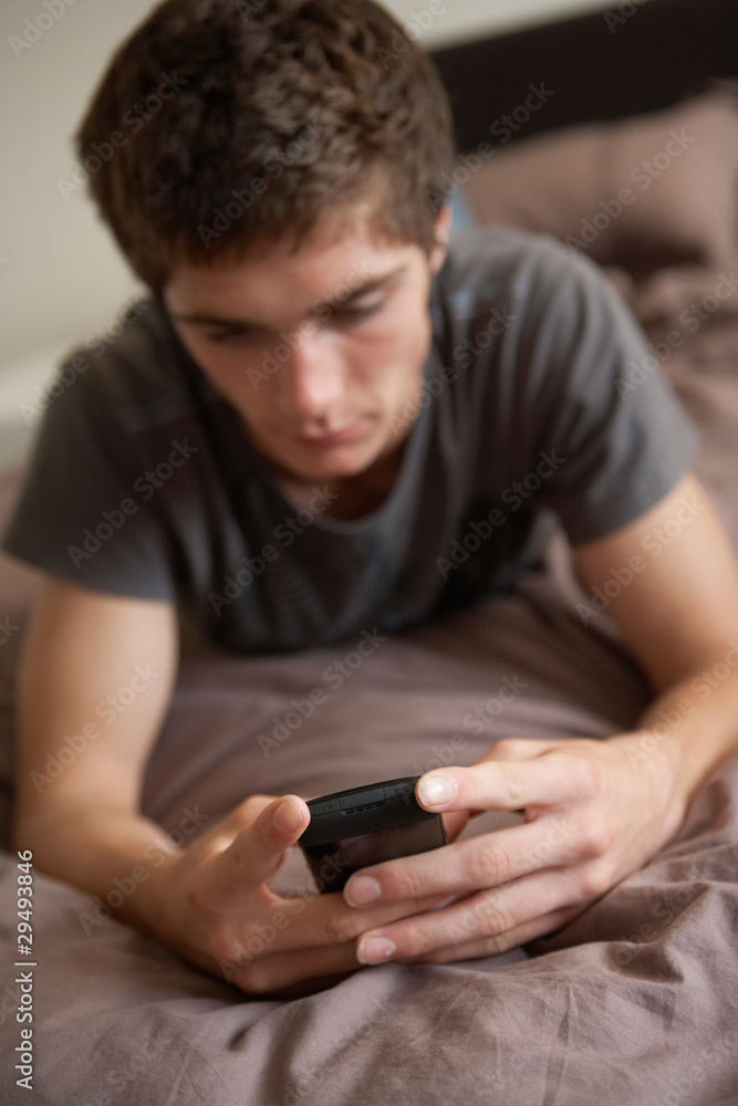 Unhappy Teenage Boy Lying In Bedroom With Mobile Phone Unhappy Teenage Boy Lying In Bedroom With Mobile Phone