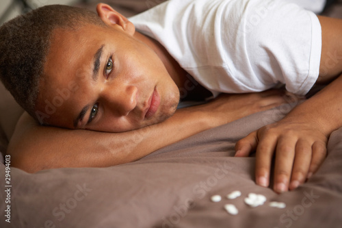 Depressed Teenage Boy Lying In Bedroom With Pills