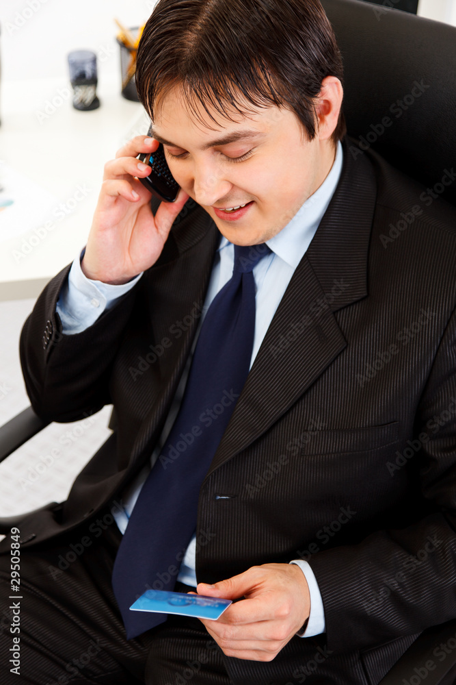 Smiling business man making purchase by phone and credit card. Smiling business man making purchase by phone and credit card.
