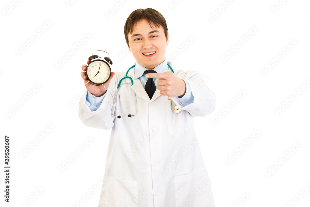 Smiling medical doctor pointing finger on alarm clock Smiling medical doctor pointing finger on alarm clock