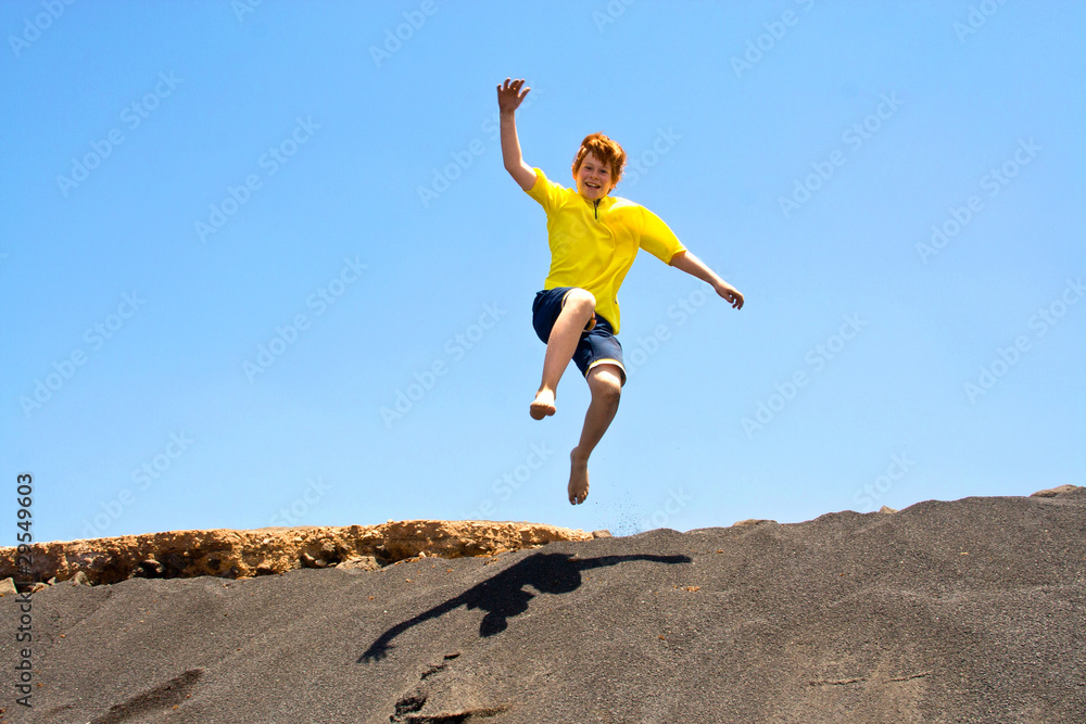 boy has fun jumping in the dunes of the beach into the ocean boy has fun jumping in the dunes of the beach into the ocean