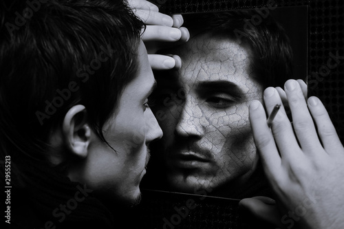 young hadsome man with cracked face looks in mirror