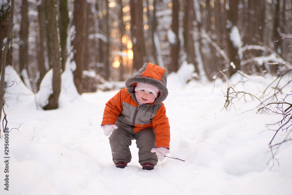 Adorable baby walking in snow winter forest try to pick up wood