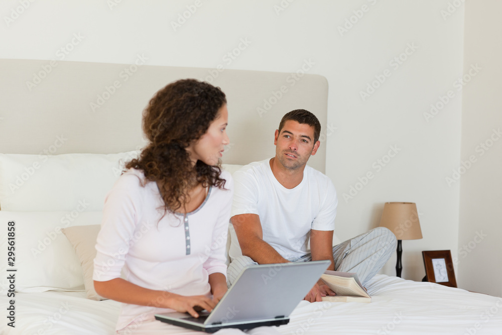 Woman working on her laptop while her husband is reading Woman working on her laptop while her husband is reading