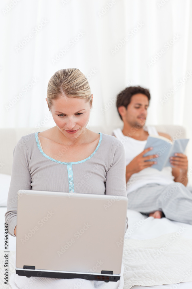 Woman working on her laptop while her husband is reading Woman working on her laptop while her husband is reading