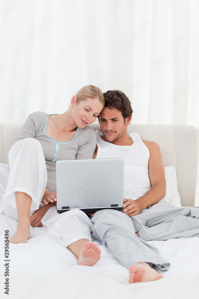 Adorable couple looking at their laptop on the bed Adorable couple looking at their laptop on the bed