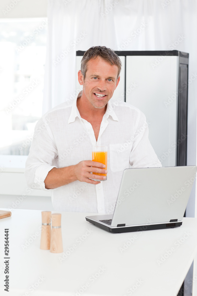 Man looking at his laptop while he is drinking oranje juice Man looking at his laptop while he is drinking oranje juice