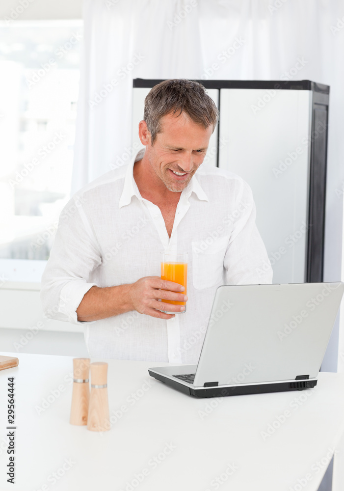 Man looking at his laptop while he is drinking oranje juice Man looking at his laptop while he is drinking oranje juice