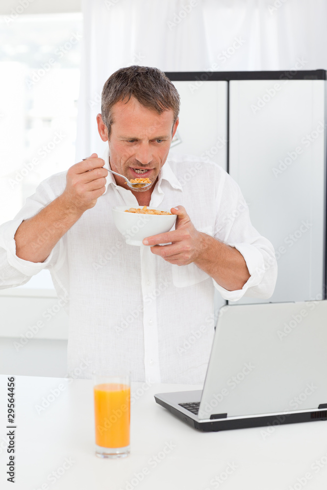 Man eating cereal while he is working on his laptop Man eating cereal while he is working on his laptop