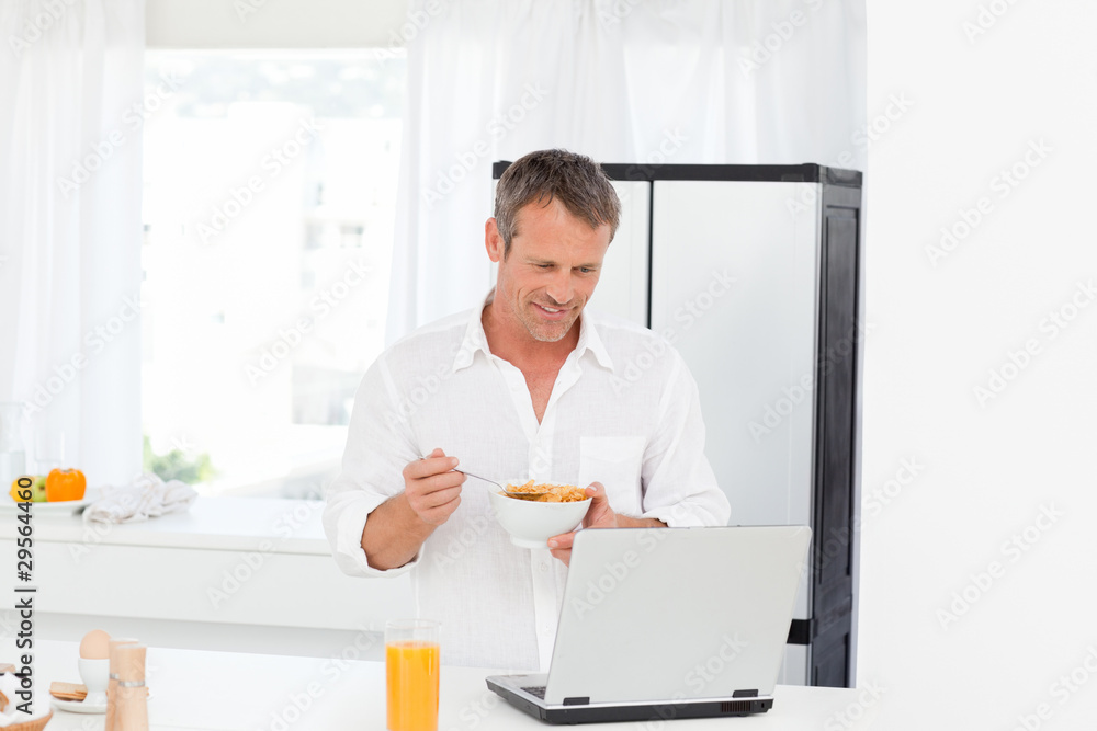 Man eating cereal while he is working on his laptop