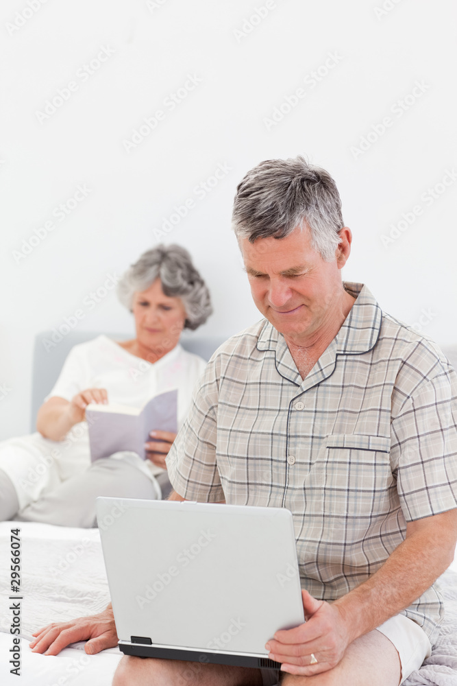 Man working on his laptop while his wife is reading Man working on his laptop while his wife is reading