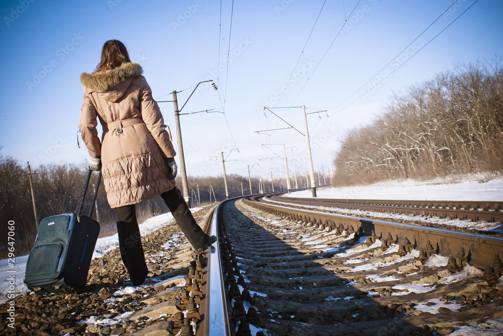 Teen girl with a suitcase near the railways at winter time