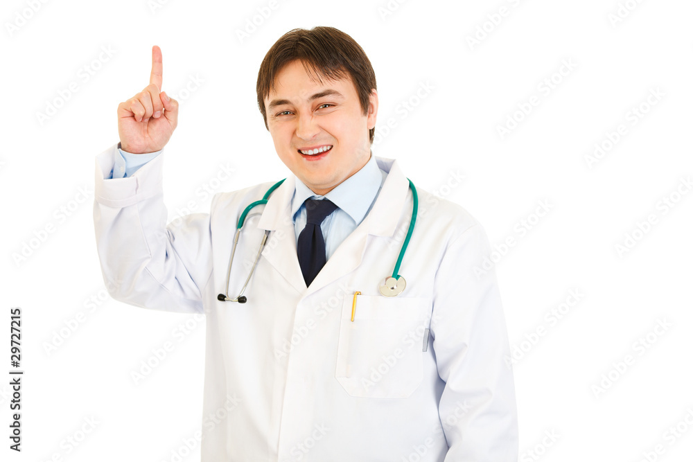 Smiling young medical doctor pointing finger up Smiling young medical doctor pointing finger up