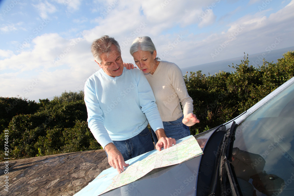 Senior couple looking at road map on car hood