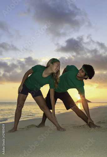 couple doing yoga, stretches, on the beach at sunrise