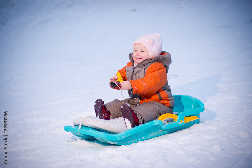 Adorable baby sliding on sleigh from hill in park and smile Adorable baby sliding on sleigh from hill in park and smile