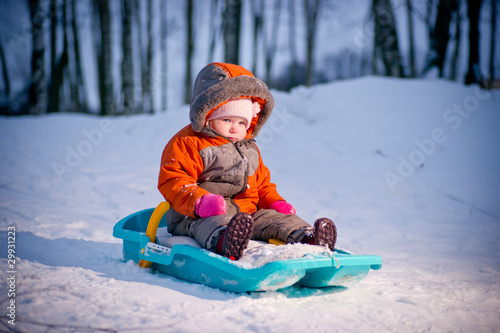 Serious cute baby sliding on sleigh from hill in park