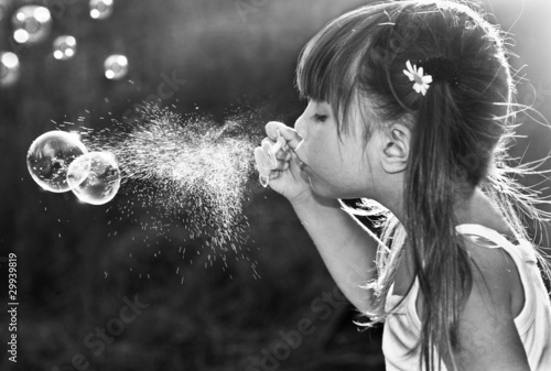 Black and white portrait of a little girl blowing soap bubbles