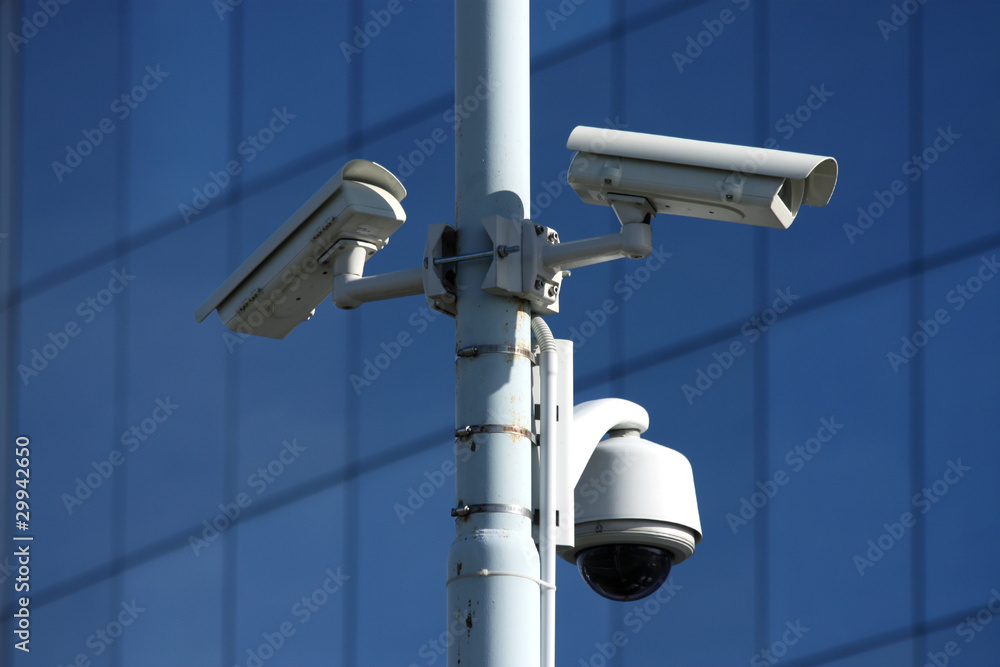three security cameras on front of glass building three security cameras on front of glass building
