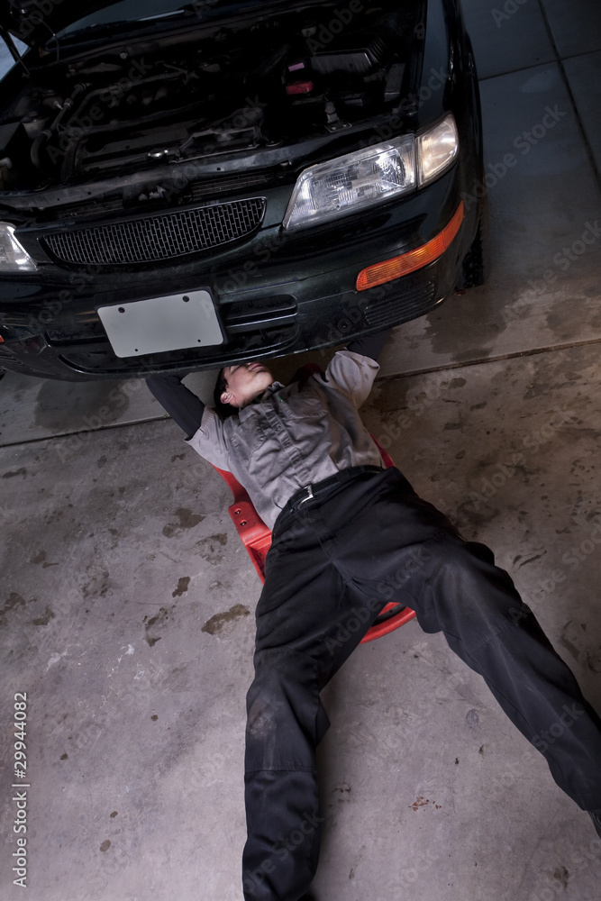 Auto mechanic working under a car repairing an engine Auto mechanic working under a car repairing an engine