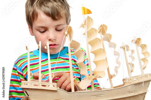 Small boy in striped shirt work with zeal on artificial ship photo