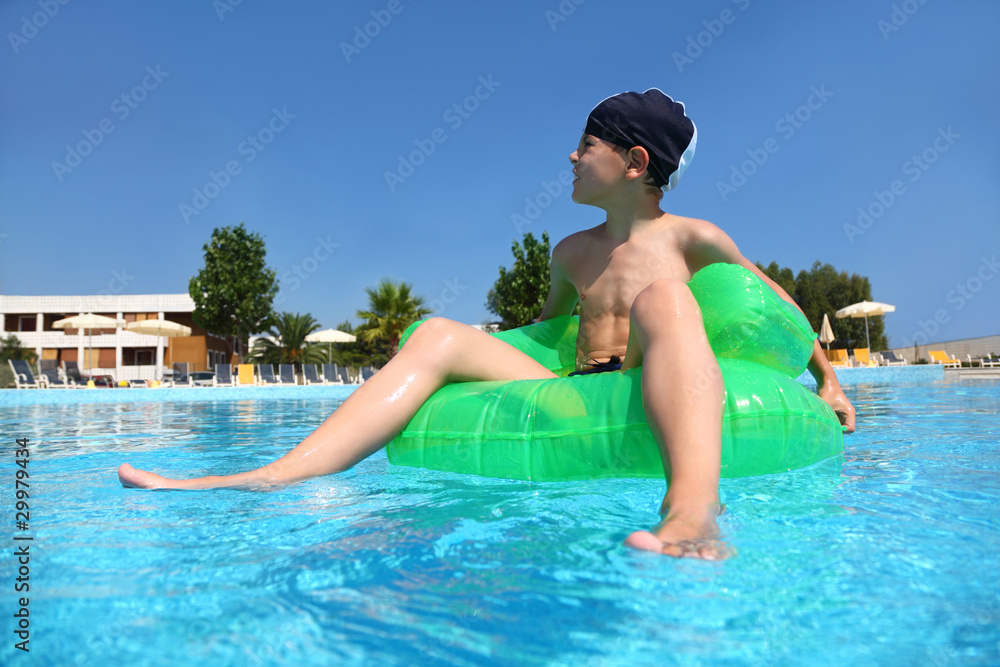 Boy sits on  green inflatable arm-chair for bathing in  pool