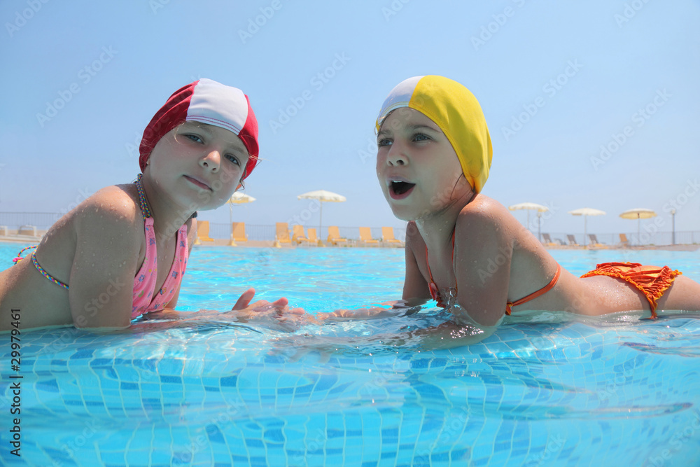 Two girls lie in  day-time in  pool opposite each other