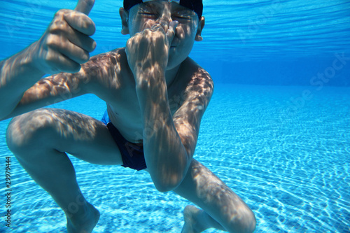 Boy dives under water in  pool and closes  nose  hand photo