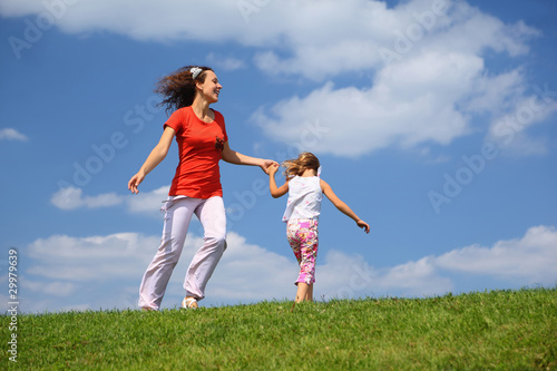 Mother with daughter hurry and play on grass in day-time