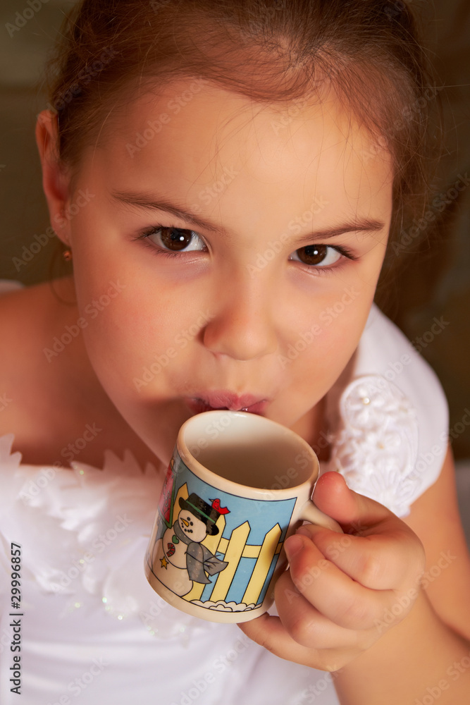 The little girl in a white dress drinks from a small cup. The little girl in a white dress drinks from a small cup.