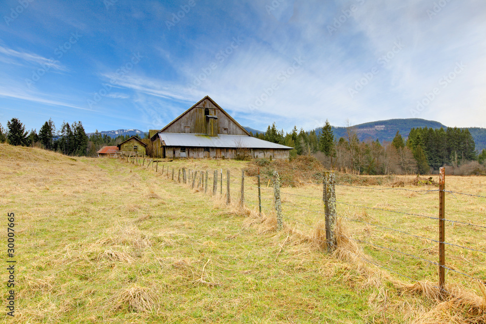Large old rustic grey barn in the field with mountain Large old rustic grey barn in the field with mountain