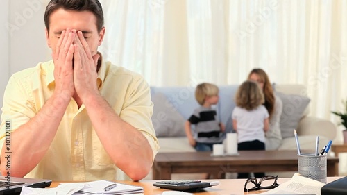 Man calculating his bills with his family in the background