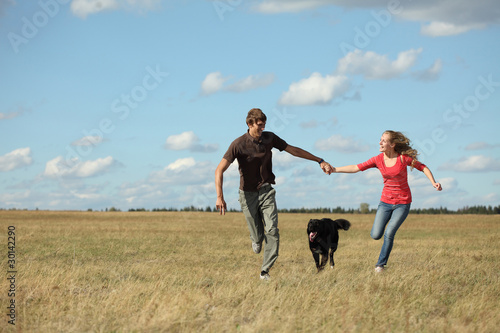Young happy family running with dog on a green meadow