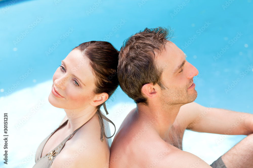 Couple sitting beside the swimming pool back to back