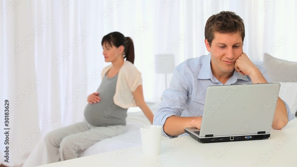 Pregnant woman stroking her belly while her boyfriend is working