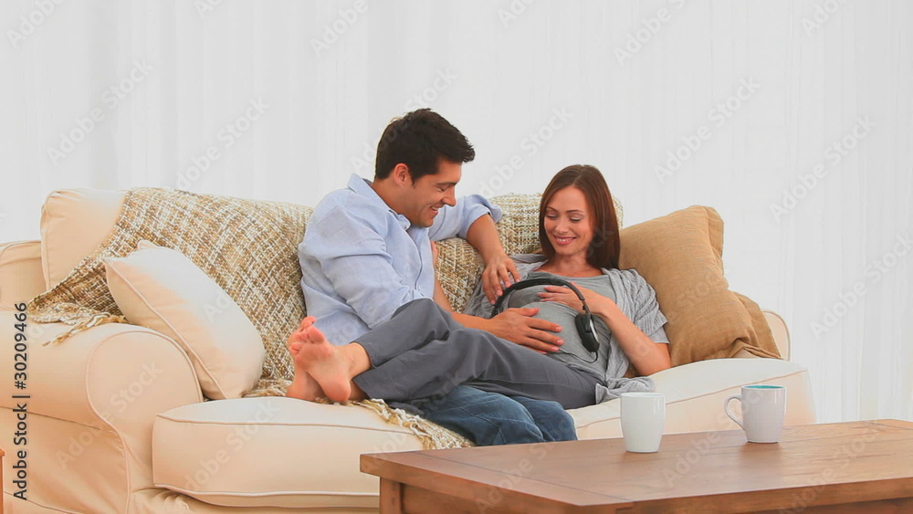 Handsome man putting headphone on the belly of his pregnant wife Handsome man putting headphone on the belly of his pregnant wife