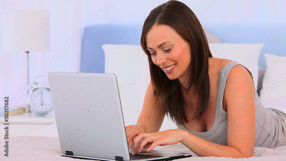 Woman laying on her bed with a laptop Woman laying on her bed with a laptop