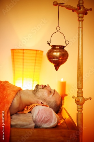 Man having a shirodhara massage in a salon photo