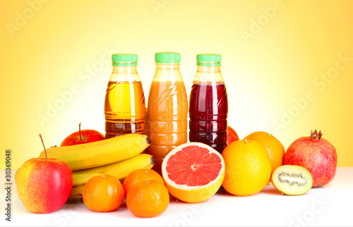 bottles of juice with ripe fruits on yellow background