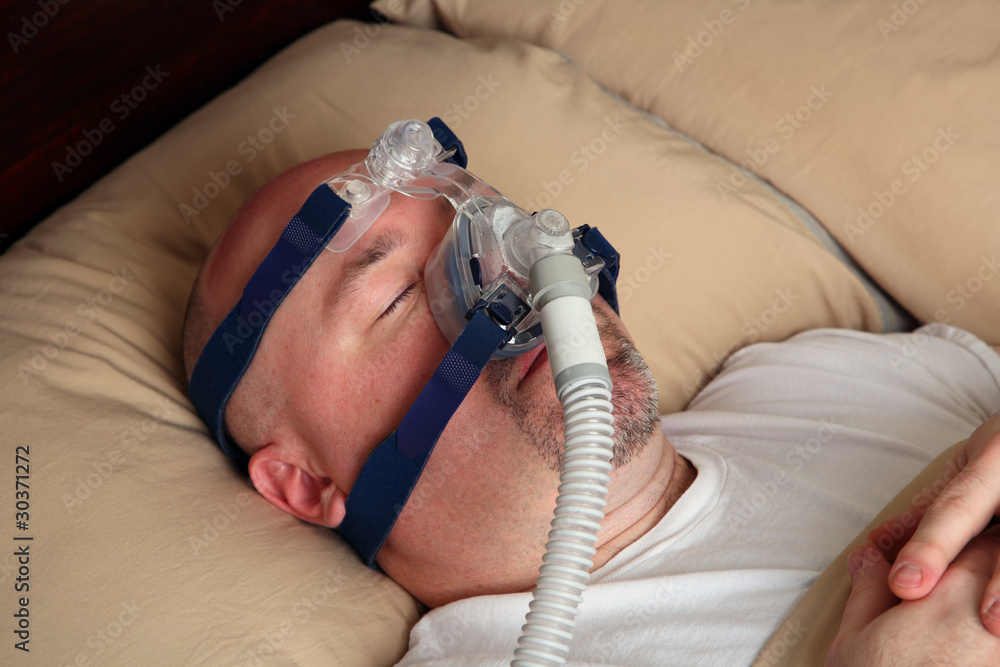 Obraz premium Man with sleep apnea using a CPAP machine in bed.
